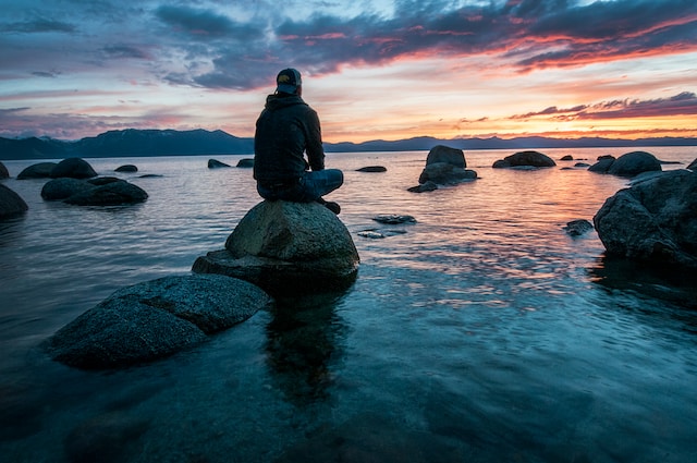 Person sitting on a stone in the ocean meditating to achieve self-awareness