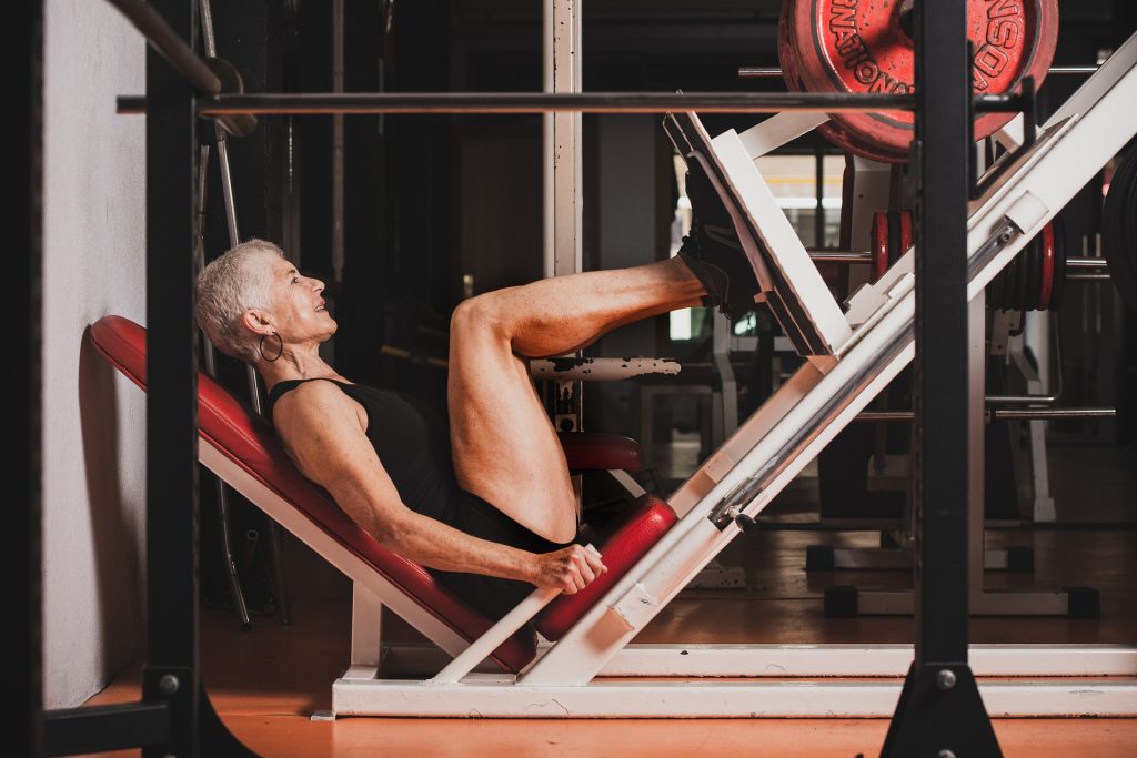 A senior woman training legs in a leg press machine.