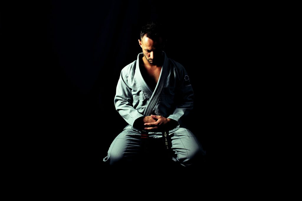 A man in a karate outfit meditating on the ground showing a form of discipline.