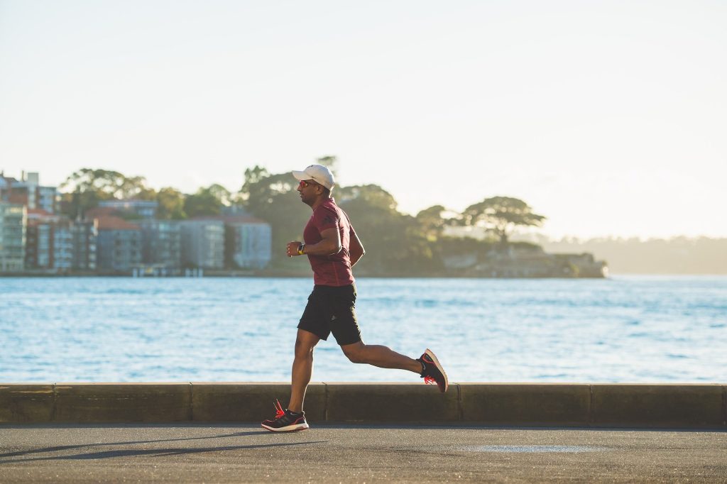 A man in running clothes running outdoors a next to the ocean on a sidewalk as form of outdoor fitness activities.