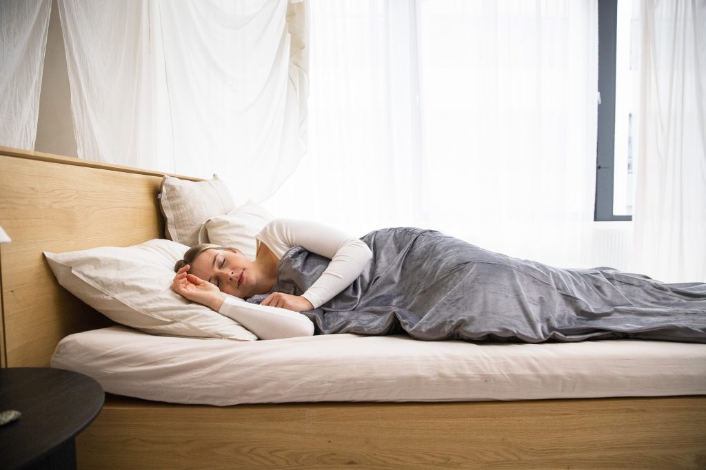 A woman sleeping in bed with a gray blanket.