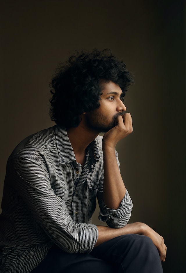 A man with curly hair sitting with his palm supporting his chin while looking away doing his daily reflections.