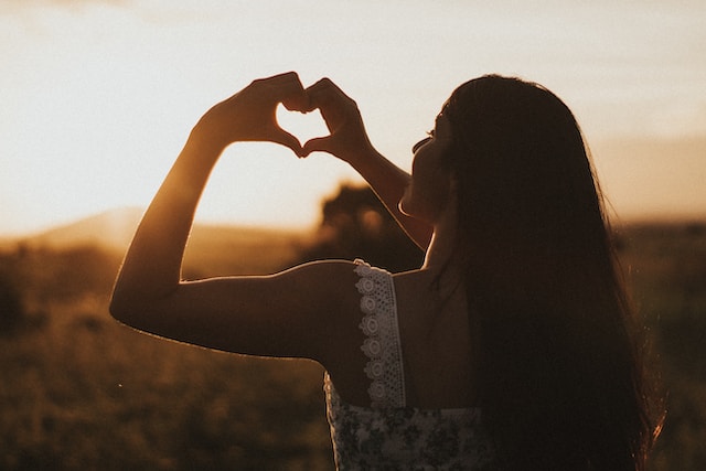 A woman making a heart with her hands which signifies self-love.