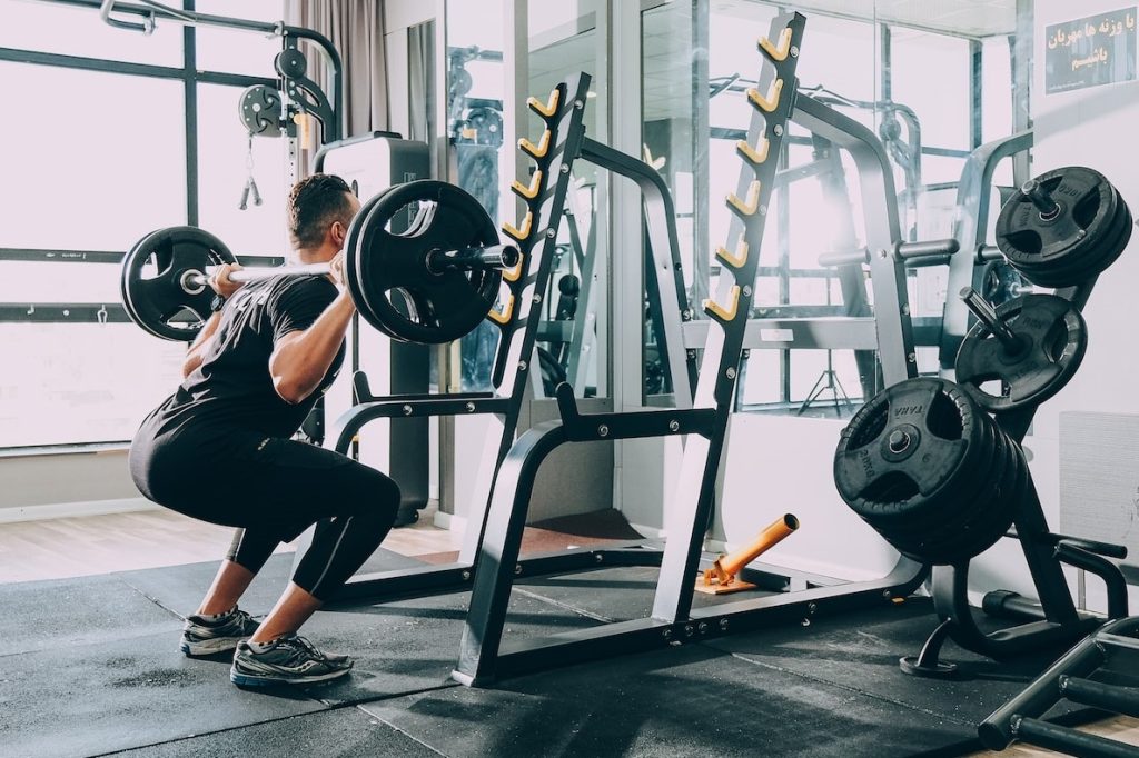 Man performing squats in a gym next to a squat rack